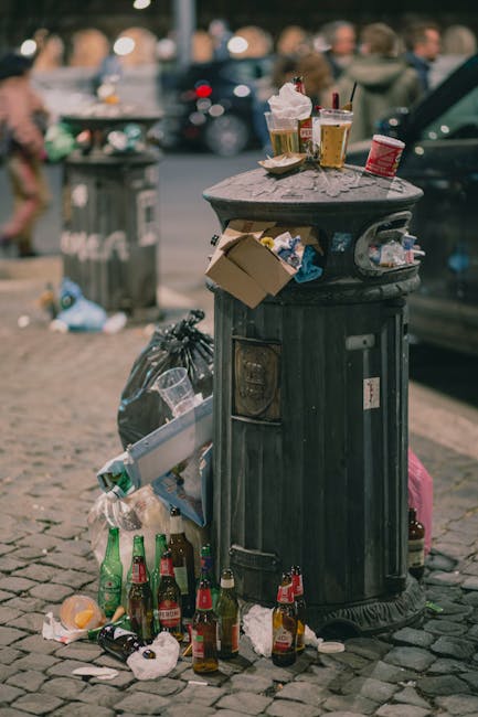 A pile of waste materials consisting of flattened cardboard boxes, some torn and with visible tape remnants, resting against a rough concrete block wall outdoors. The cardboard varies in size, with so